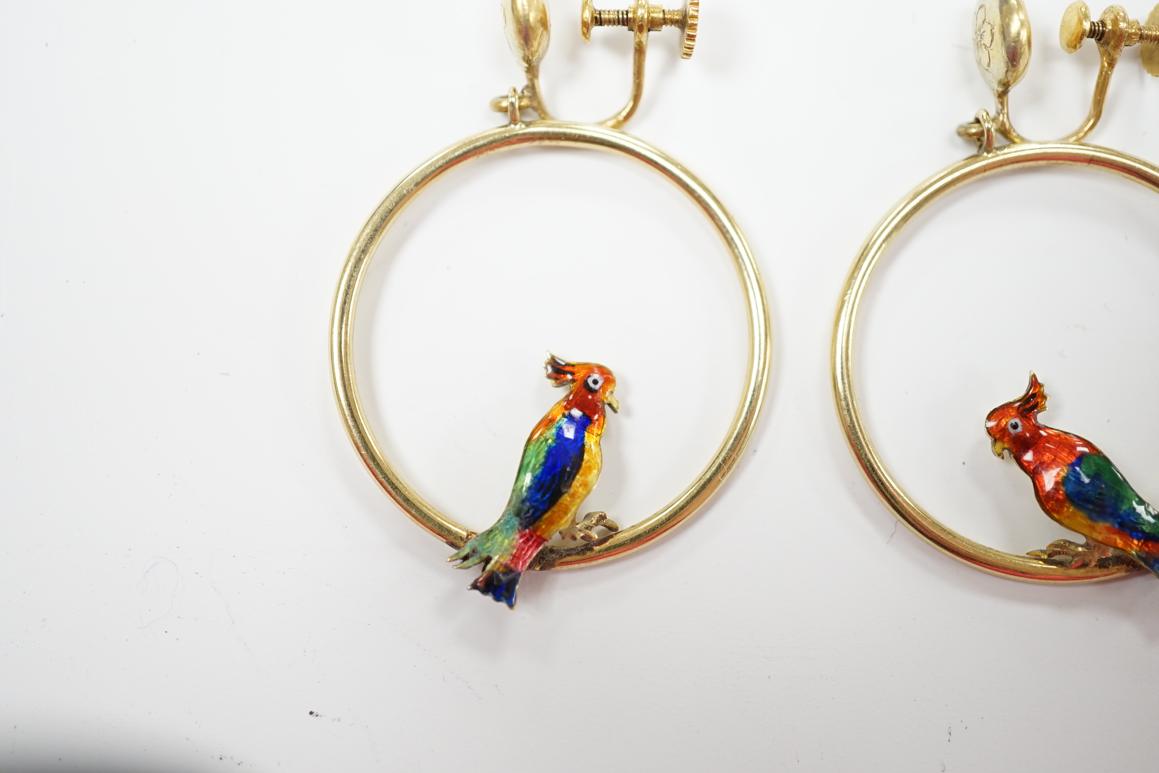 A pair of early 20th century 15ct loop ear clips, with a polychrome enamelled parrot perched upon each, diameter 30mm, gross weight 7.3 grams.
